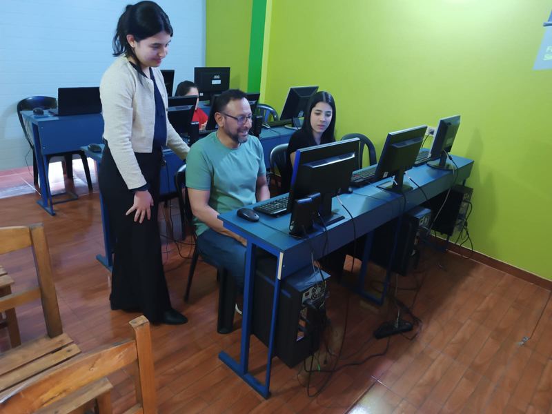 Un alumno adulto recibe ayuda de la profesora frente a su computadora.