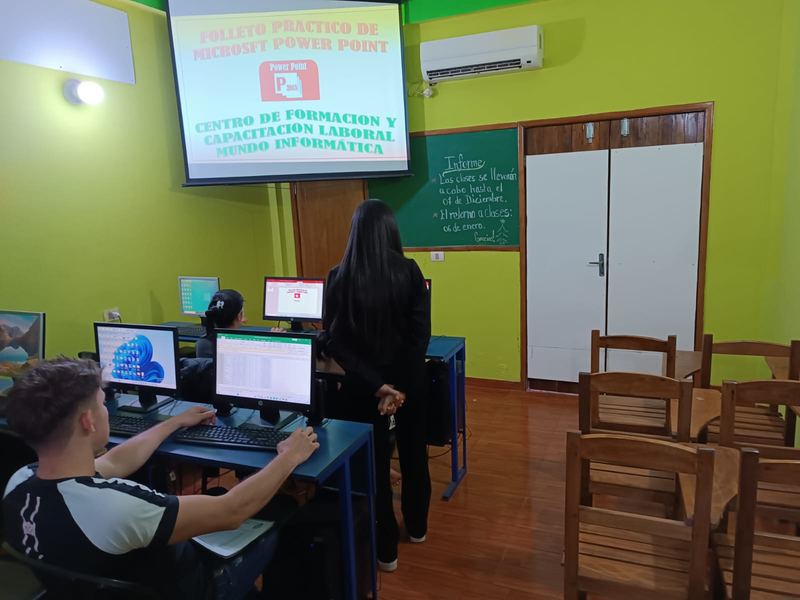 Clase de PowerPoint: la pantalla proyecta el material y la profesora acompaña.